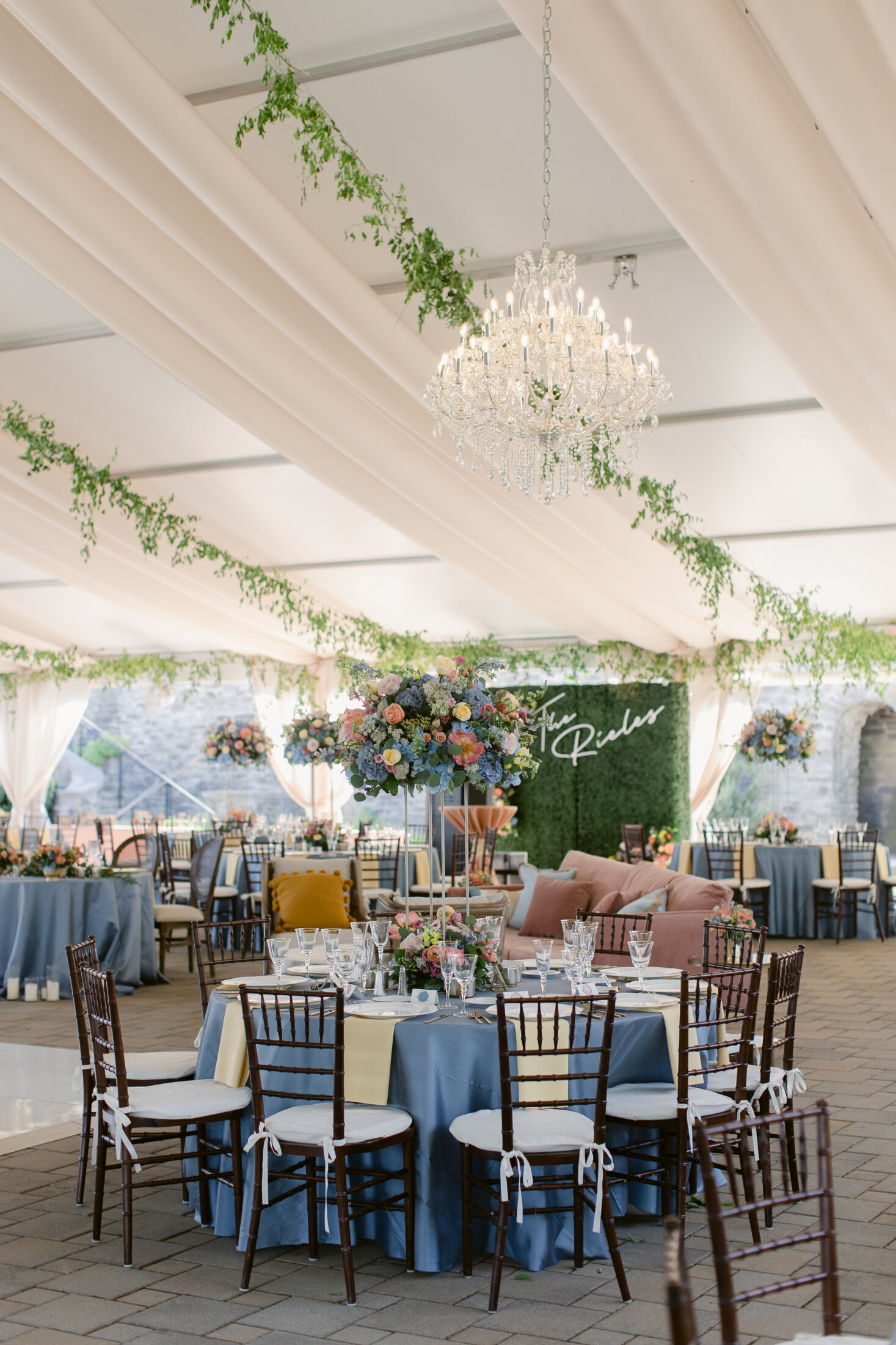 Greenery hanging in the tent at Green Acres with chandeliers and tall  flower centerpieces - Floral V Designs