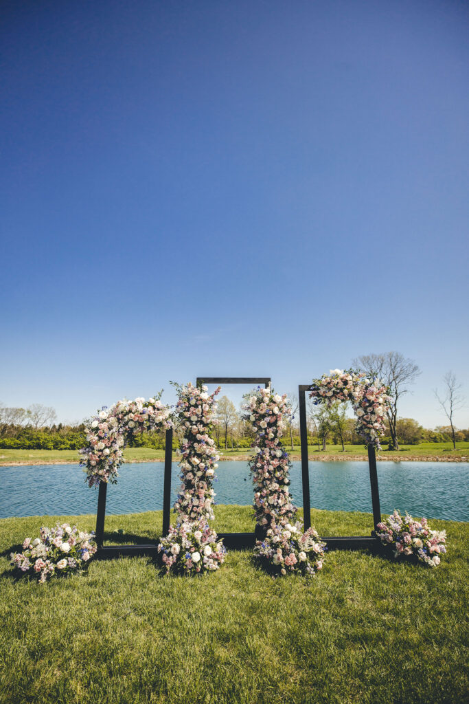 Three wedding arches with spring florals on each of them. They are set in front of the lake